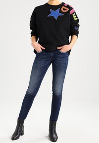 Czarna bluza z dużą niebieską gwiazdą i kolorowymi detalami. Zestawiona z ciemnoniebieskimi skinny jeansami i czarnymi botkami za kostkę.
