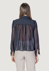 Marineblauwe transparante blouse met een effen schouderstuk, geplooide achterkant en knoopmouwen. Heeft een zachte textuur en een licht vloeiende silhouette.