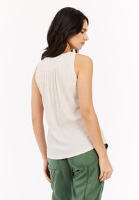 Top senza maniche di un leggero beige con tessuto texturizzato e schiena arricciata. Abbinato a pantaloni verdi larghi, per uno stile casual.
