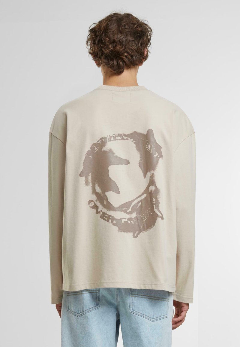 Beige Langarmshirt mit einem runden Grafikdruck auf der Rückseite. Bietet eine lockere Passform und ein weiches Baumwollmaterial. Lässiger Stil mit herabgesetzten Schultern.