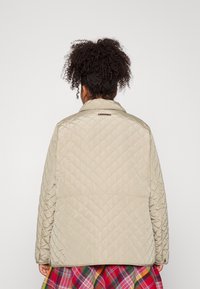 Beige vävd jacka med rak passform, med en snedkrage och en subtil märkestagg på baksidan. Texturerad yta med diamantmönster.