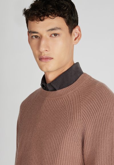 Genoppter, rostfarbener Pullover mit gerippter Textur und Rundhalsausschnitt, über einem dunklen Hemd mit Kragen getragen. Glattes Material, taillierte Form.