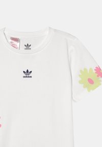 Biała bawełniana koszulka z granatowym logo Adidas na piersi oraz dużymi pastelowymi wzorami kwiatów w odcieniach różu i zieleni na rękawach.