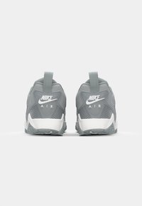 Tenisi gri Nike Air cu un upper texturat, accente albe, călcâi pronunțat și tab de prindere la spate. Caracteristică a unor tălpi din cauciuc contrastante.