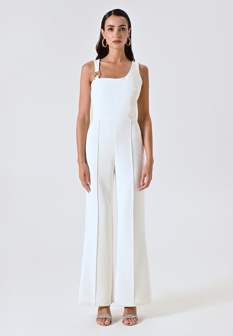 Jumpsuit blanc avec un buste ajusté, des pantalons larges et une seule bretelle avec un accent doré. Texture lisse avec des détails de couture.