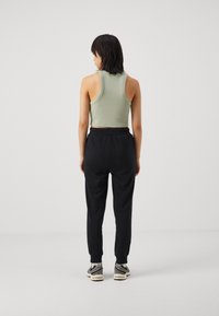 Hellgrünes, geripptes Cropped Top, kombiniert mit schwarzen, schmal zulaufenden Sweatpants mit elastischen Bündchen und lässiger Passform. Sneakers mit grau-weißen Akzenten.