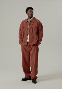 Hnedo-oranžová kordová bunda a zodpovedajúce nohavice s gombíkovým zapínaním, dvoma náprsníkovými vreckami a uvoľneným strihom. Nosí sa s ľahkým tričkom.