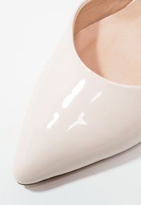 Chaussure à talon haut pointu beige brillant montrant l'avant et la doublure intérieure sur fond blanc.