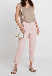 Beige bezramenný top s krajkovým lemem, růžové zúžené kalhoty, stříbrné sandály a malá bílá kabelka s kruhovým detailem.