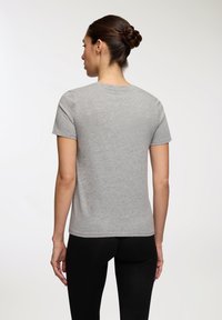 Szara bawełniana koszulka z krótkim rękawem, okrągłym dekoltem i luźnym krojem, widok z tyłu, zestawiona z czarnymi legginsami.