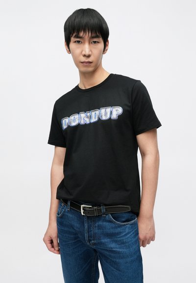 T-shirt noir en coton avec l'inscription "DON DUP" en lettres bleues métalliques épaisses. Associé à un jean en denim bleu et une ceinture noire.