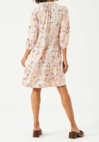 Sukienka w kwiaty z różowym tłem, rękawami o długości trzech ćwiartek i warstwowym krojem. Wykonana z lekkiego materiału z wyrazistymi, wielokolorowymi wzorami.