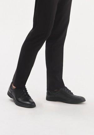 Czarne skórzane buty o gładkiej fakturze, okrągłym nosku i sznurowanym fasonie. W połączeniu z wąskimi czarnymi spodniami. Minimalistyczny i nowoczesny wygląd.