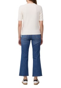 Top crème à manches courtes côtelé associé à un jean bleu évasé taille haute. La tenue est complétée par des baskets blanches décontractées avec des accents noirs.