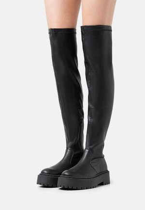 Botas de cuero negras hasta la rodilla con una textura suave, suela de plataforma gruesa y detalle de cremallera lateral. Diseño minimalista con una silueta elegante.