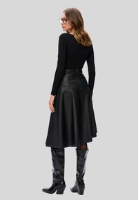 Czarny top z długim rękawem zestawiony z czarną skórzaną spódnicą midi oraz błyszczącymi, czarnymi kozakami za kolano, z detalem w postaci zamka z tyłu spódnicy.
