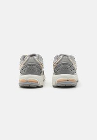 Une paire de baskets de sport grises et blanches vue de l'arrière sur un fond blanc uni.