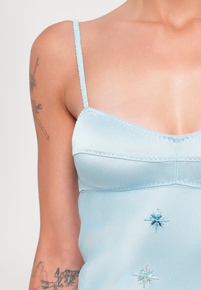 Top de satén azul claro con tirantes delgados y texturizados, que presenta adornos de cuentas azules en forma de estrella. Tejido suave con detalles de costura delgada.