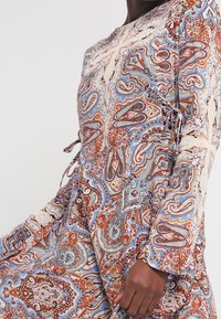 Robe à manches longues en tissu fluide présentant un motif cachemire coloré avec des nuances de bleu, d'orange et de crème ; accents noués à la taille.