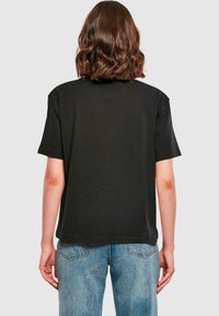 Sort kortærmet T-shirt med afslappet pasform, lavet af blødt bomuld, med rund halsudskæring og lige kant. Denimbukser synlige.
