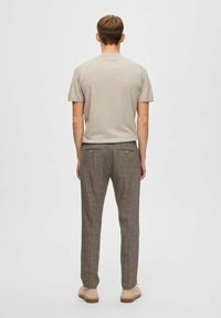 Chemise beige à manches courtes et pantalon à carreaux gris. Coupe décontractée, texture douce, avec deux poches à l'arrière et chaussures marron clair.