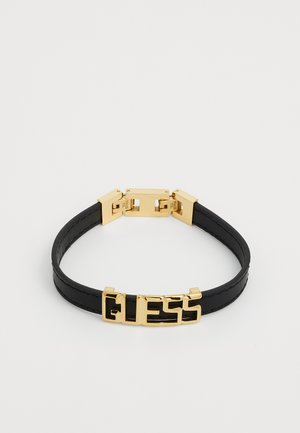 Black leather bracelet with a gold-tone metal clasp featuring embossed "GUESS" logo. Smooth texture, sleek design, and minimalist aesthetics.