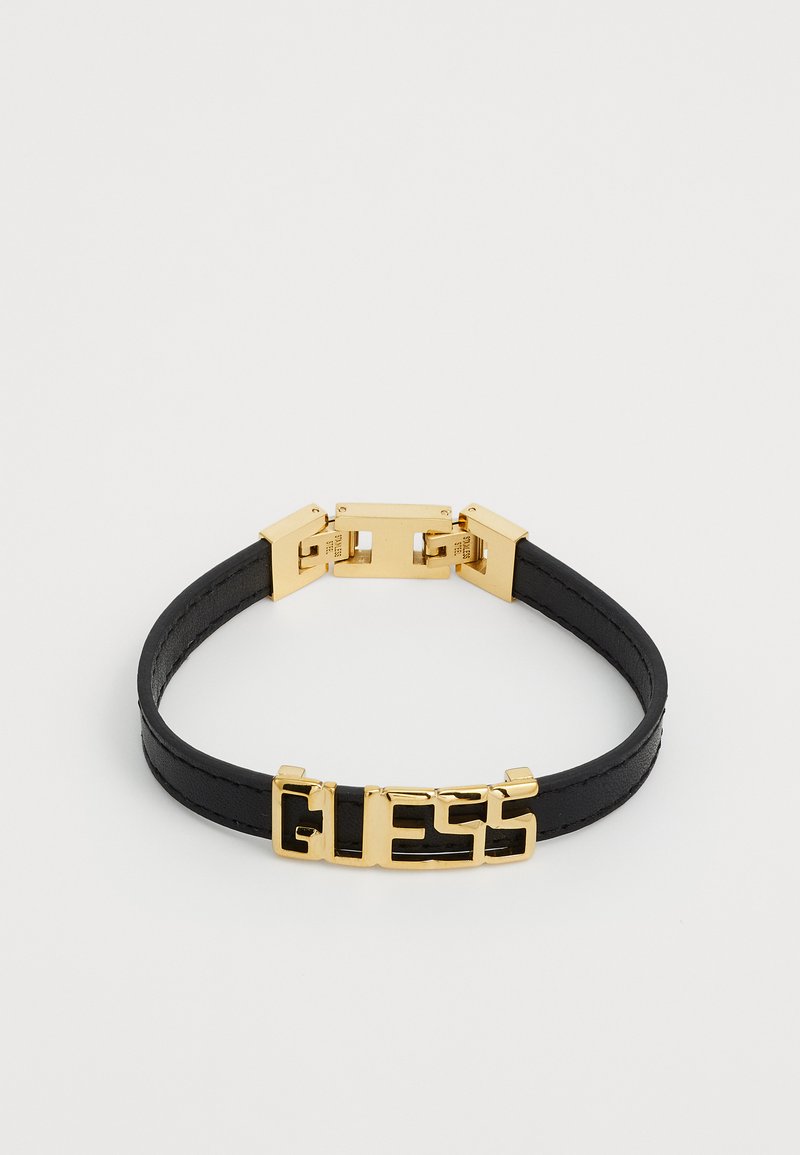 Pulsera de cuero negra con un cierre de metal en tono dorado que presenta el logotipo "GUESS" en relieve. Textura suave, diseño elegante y estética minimalista.