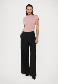 Top ajustado de color rosa claro con mangas cortas, combinado con pantalones negros de pierna ancha y cintura alta. Diseño sencillo y texturas suaves.