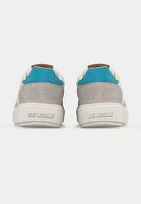 Ζευγάρι μπεζ και γκρι αθλητικά παπούτσια με τιρκουάζ ταμπελάκια στη φτέρνα και τη φράση «LOVE MOSCHINO» χαραγμένη στις λευκές σόλες, από πίσω.