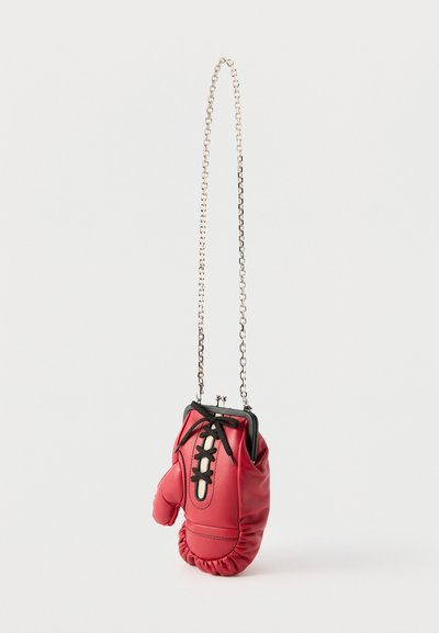 Κόκκινο δερμάτινο πορτοφόλι σε σχήμα γαντιού του μποξ με μαύρο κορδόνι δαντέλας και ασημένιο λουράκι αλυσίδας, κρεμασμένο μπροστά σε λευκό φόντο.