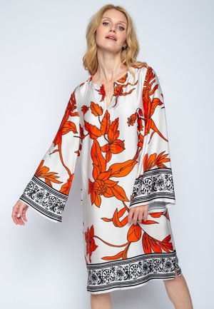 Blumen-Tunika-Kleid aus weißem Stoff, mit kräftigen orangen Blumen, schwarzen Akzenten an den Ärmeln und dem Saum sowie einem V-Ausschnitt.