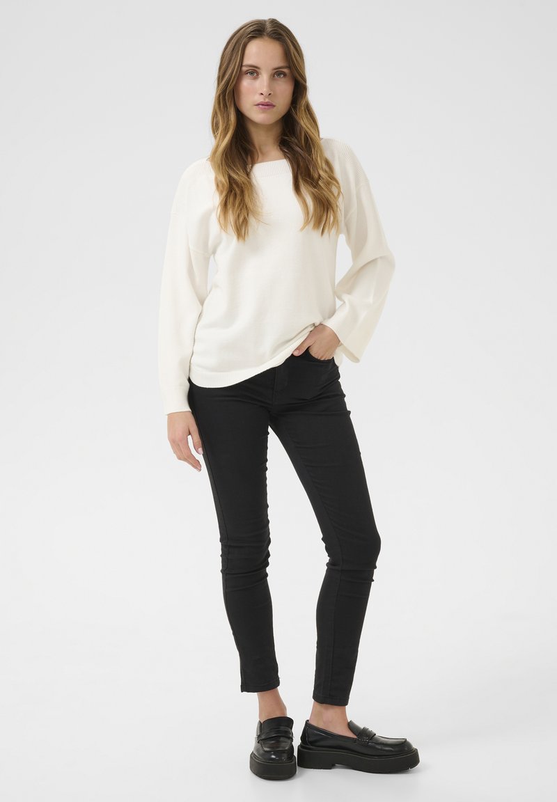 Krämfärgad stickad tröja med fyrkantig halsringning, långa ärmar, kombinerad med åtsittande svarta jeans och kraftiga svarta loafers. Minimalistisk stil.