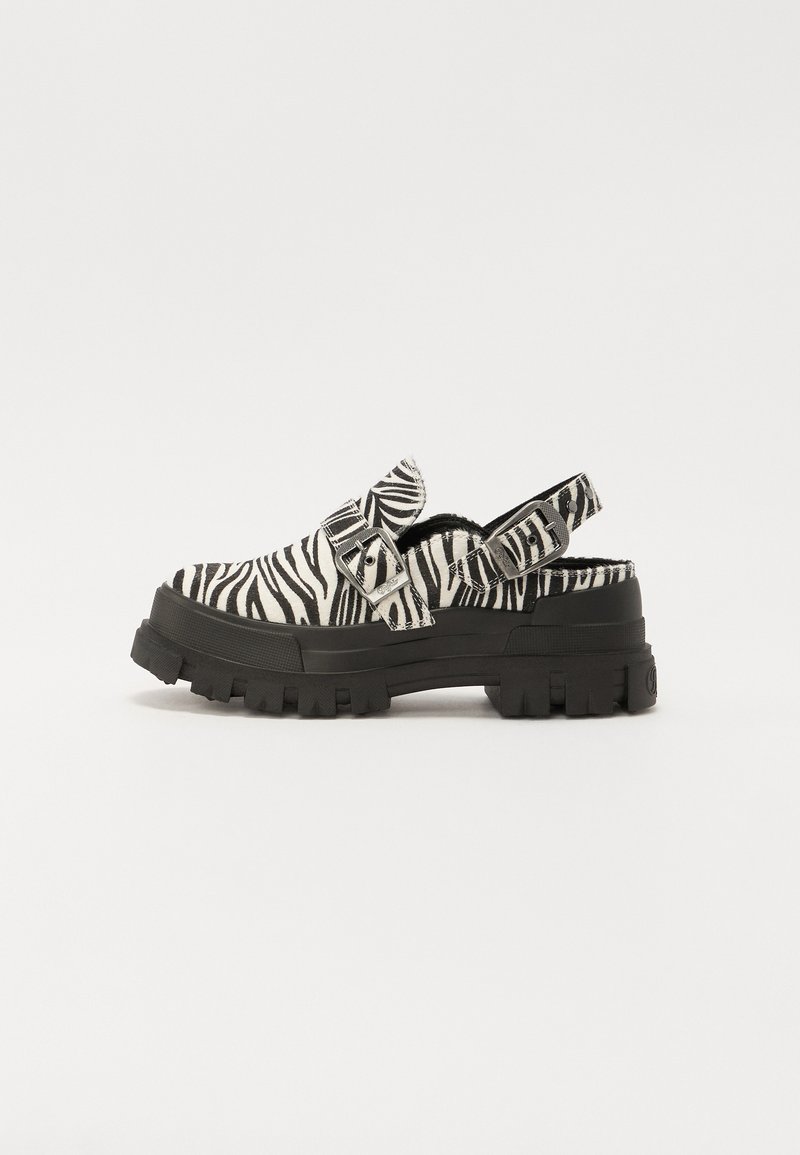 Tamancos com padrão de zebra em preto e branco, com sola preta robusta, alça ajustável e textura suave no material superior.