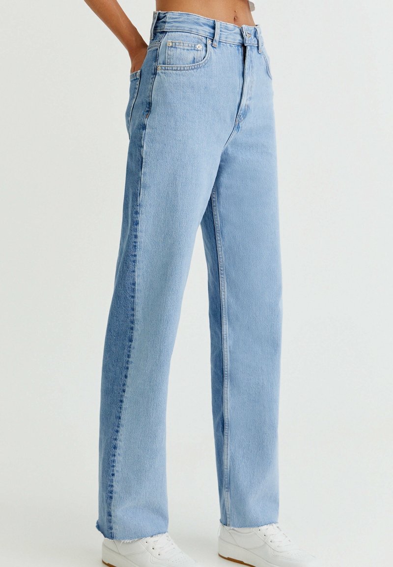 Jean en denim bleu clair avec une taille haute, une coupe droite et un ourlet effiloché. Il présente des passants de ceinture, des poches avant et une braguette zippée.