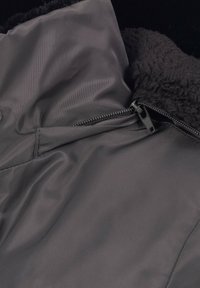 Graue Jacke mit einem glatten Außenmaterial und einem weichen, fuzzy schwarzen Innenfutter. Mit Reißverschluss und Knopfverschluss, lockere Passform.