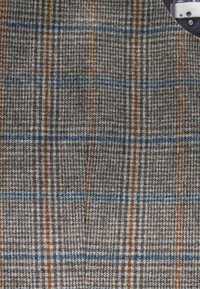 Wollstoff mit einem karierten Muster in Braun, Blau und Weiß. Die Textur ist grob, mit sichtbarem Gewebe und kontrastierenden Streifen.