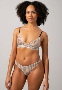 Soutien-gorge et bikini en tissu beige transparent avec des pois noirs. Présente des fines bretelles noires et un design triangulaire élégant.