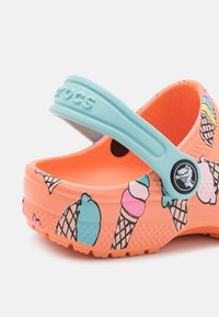 Crocs naranja brillante con patrones de conos de helado, correa azul y suelas texturizadas. Material suave; diseño ligero y resistente al agua.