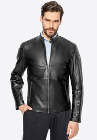 Giacca in pelle nera con colletto alto, zip frontale e dettagli trapuntati sulle spalle; texture liscia e vestibilità sartoriale.