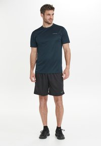 Miestenska športová súprava pozostávajúca z tmavomodrej košele s krátkym rukávom a čiernych šortiek. Obsahuje ľahký, vlhkosť odvádzajúci materiál a jednoduchý dizajn.