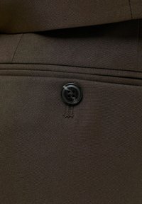 Gros plan sur un tissu brun foncé avec un bouton noir à quatre trous et des coutures visibles sur un vêtement sur mesure.