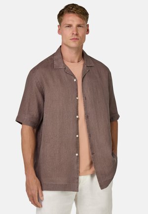 Chemise à manches courtes, boutonnée, en mélange de lin de couleur marron discret avec une finition texturée ; dotée d'un col et de poches sur les côtés. Portée sur un t-shirt rose clair.