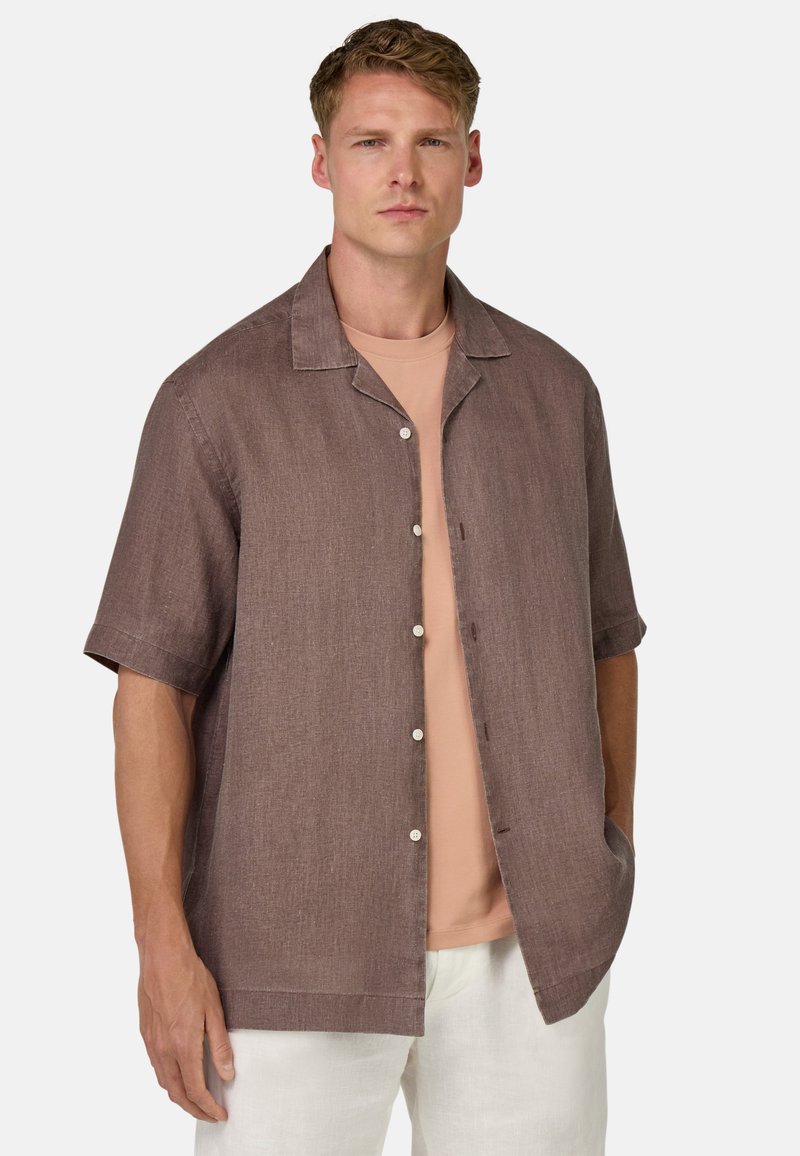 Camicia a maniche corte, con bottoni, di un marrone tenue, in misto lino con una finitura testurizzata; presenta un colletto e tasche laterali. Indossata sopra una maglietta rosa chiaro.
