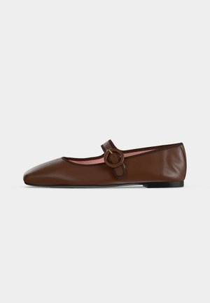 Chaussure plate Mary Jane en cuir marron avec bride à boucle ronde et semelle noire sur fond gris clair.
