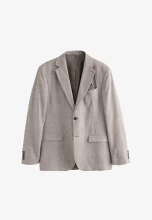 Homme ajustant la manche d'un blazer à carreaux marron avec des boutons noirs et le poignet de chemise blanc visible.