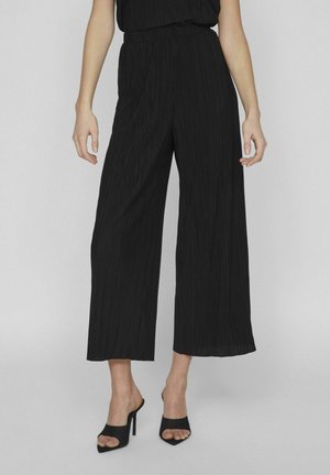 Pantalons larges noirs avec une texture plissée, dotés d'une taille élastique et associés à des mules à talons ouverts noires.