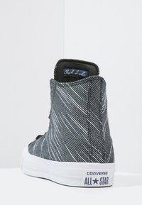 Zapatilla alta de lona a rayas en blanco y negro, con suela de goma blanca, que presenta un collar acolchado y el logo "Chuck Taylor" en la lengüeta.