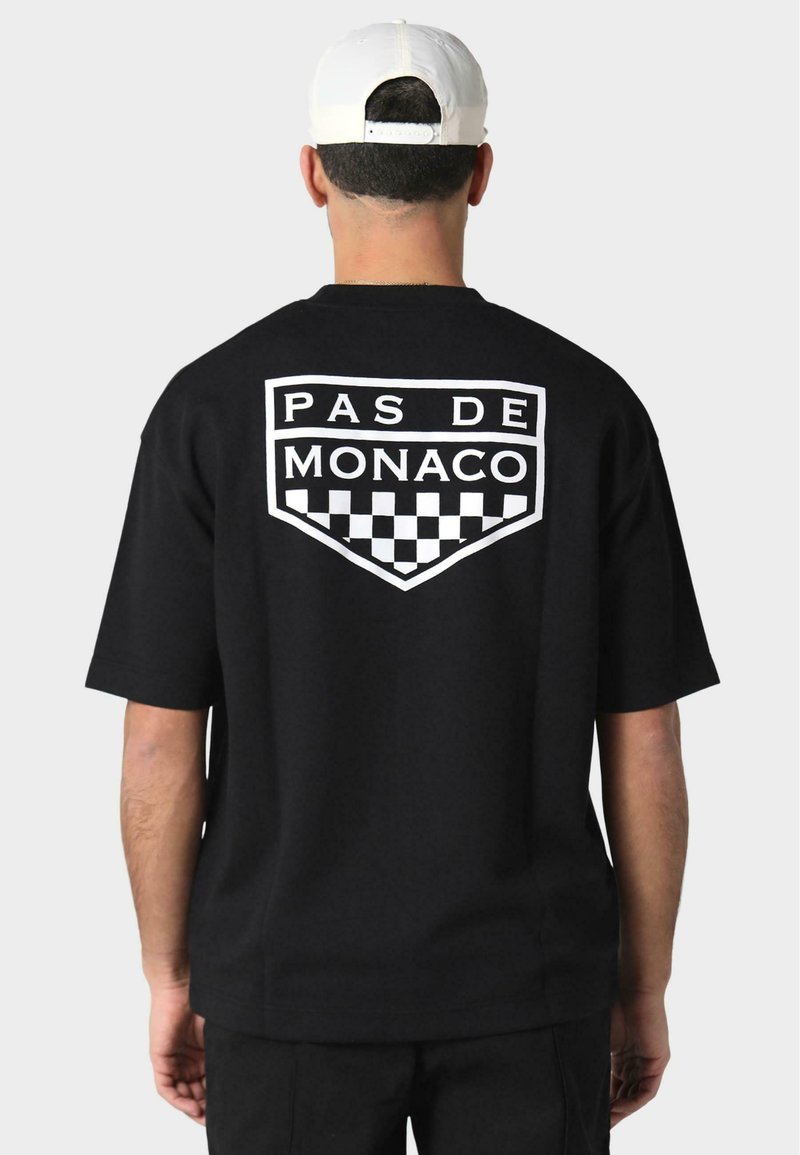 Melna īsām piedurknēm t-krekls ar lielu baltu "PAS DE MONACO" logo un kvadrātveida rakstu aizmugurē, izgatavots no mīksta kokvilnas auduma.