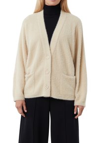 Kremowy kardigan o teksturowanym wykończeniu, luźnym kroju, dekoltem w serek i zapięciem na guziki z przodu. Posiada dwie przednie kieszenie.