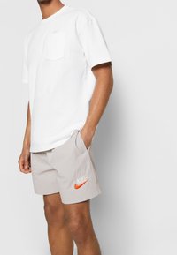 White cotton t-shirt with a pocket and short sleeves paired with light gray textured shorts featuring an orange Nike logo and side pockets.